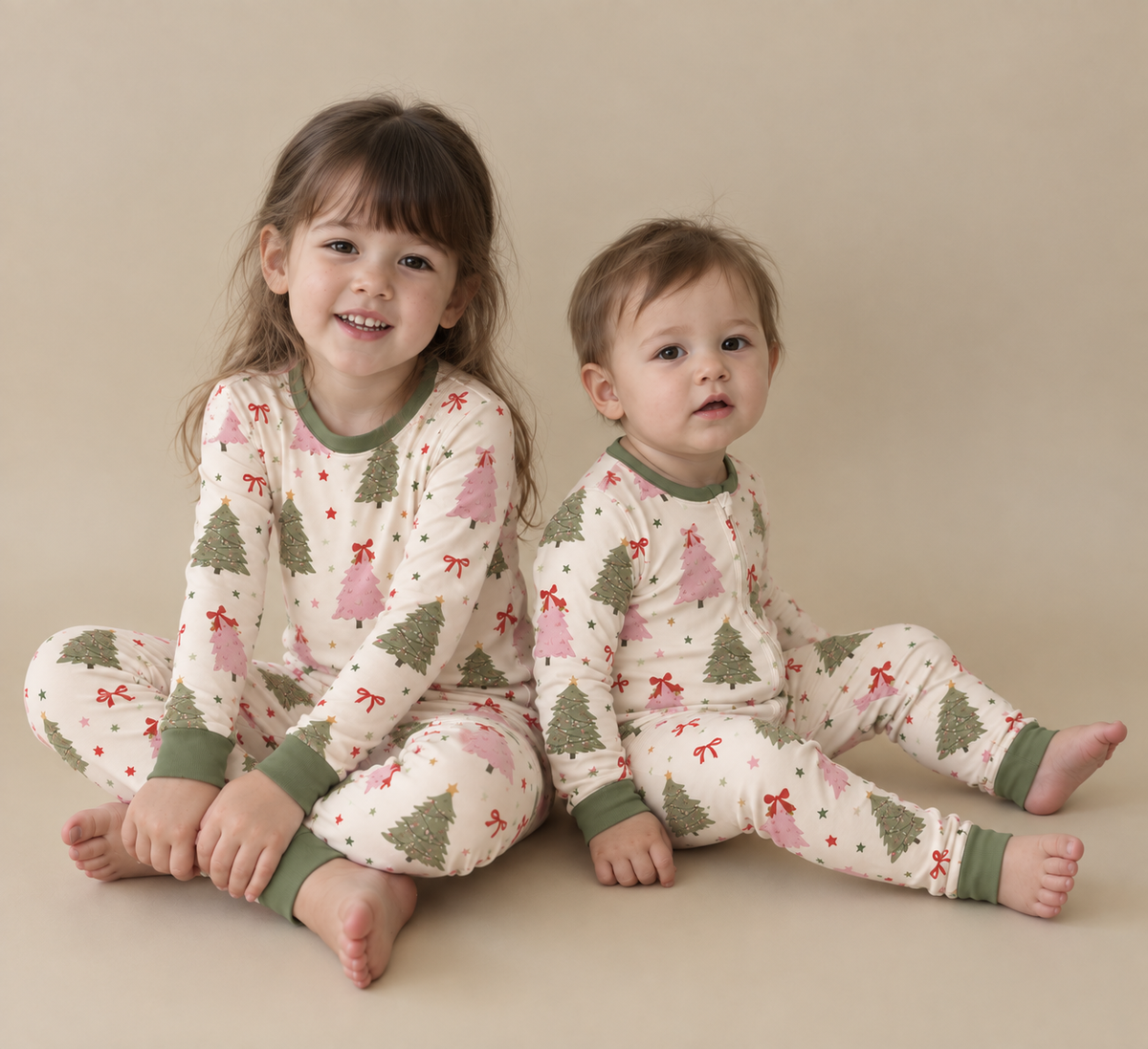 Big sister and toddler sitting together in Christmas Tree bamboo pajamas with sage green and pink trees, red bows and sage green cuffs