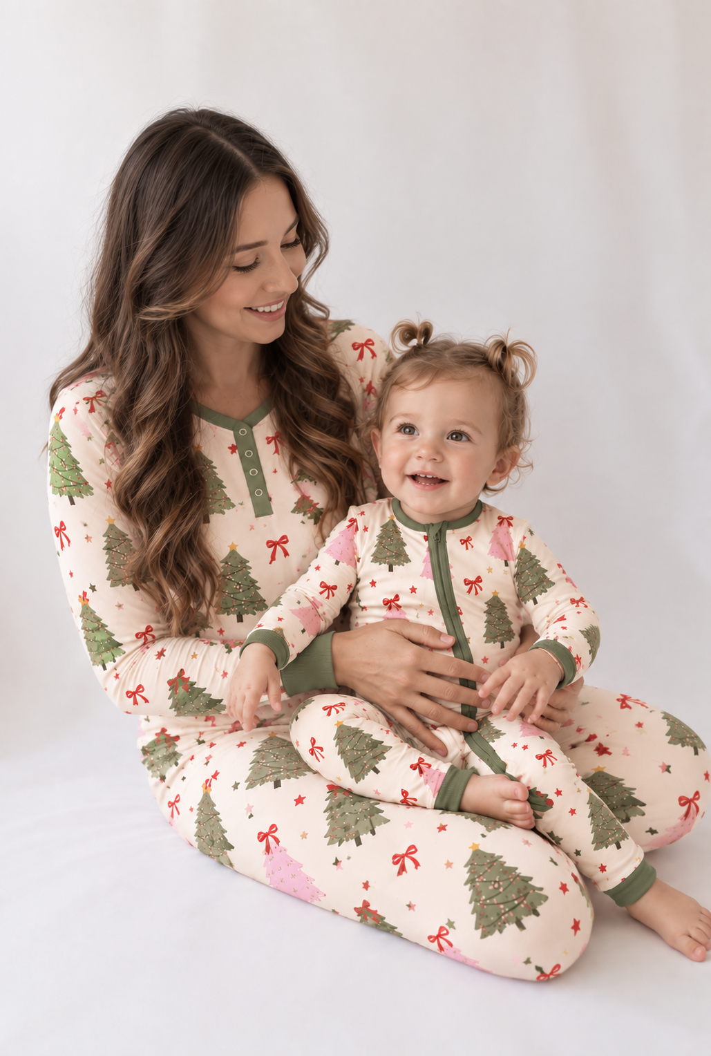 Mom in Christmas Tree women's bamboo pajamas holding her toddler in the matching zippy, sage and pink trees on cream