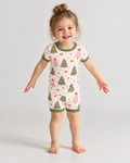 Smiling toddler in Christmas Tree short sleeve bamboo pajamas, a cream tee and shorts with sage green and pink trees, red bows and sage green trim