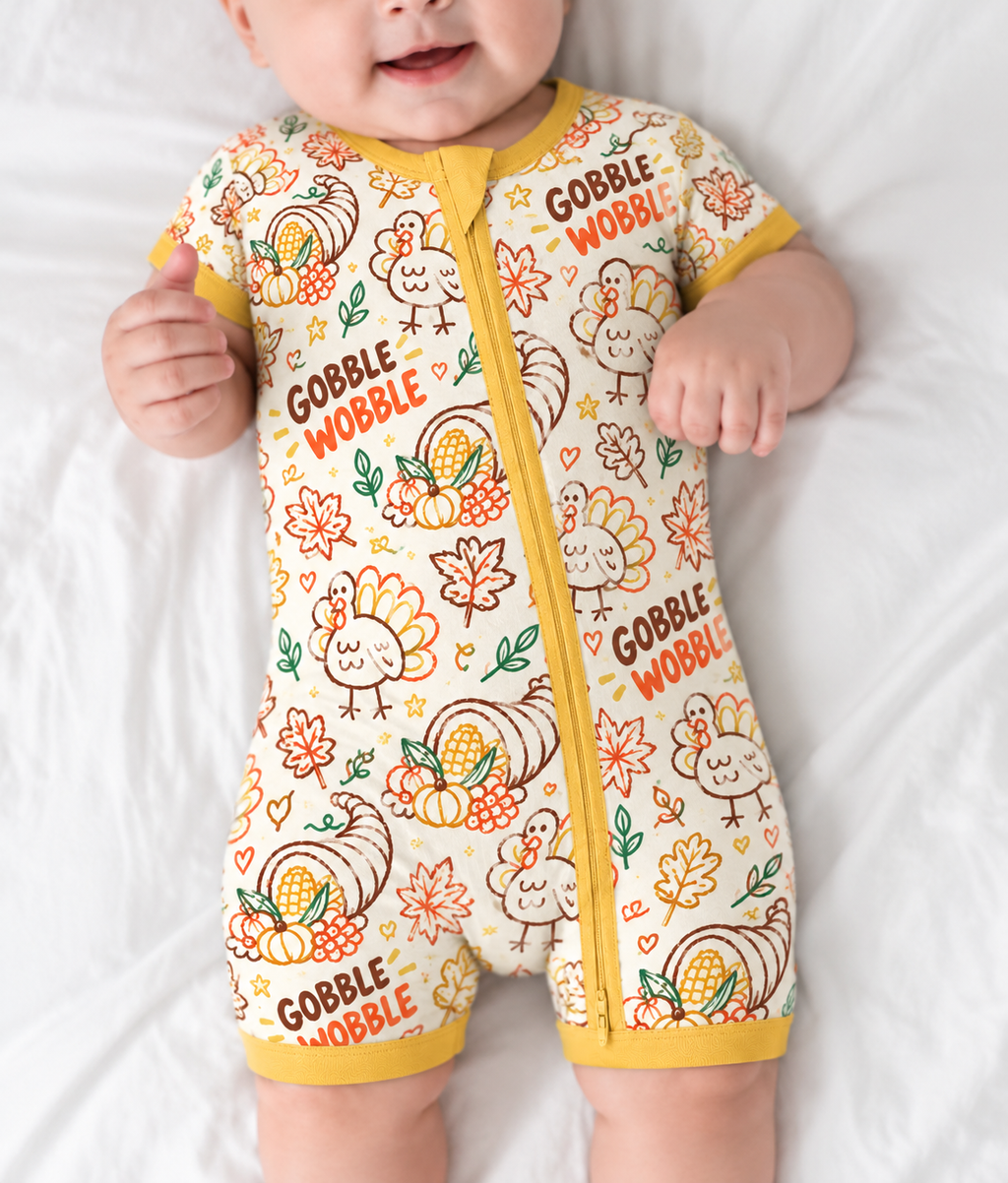 Baby lying down in the Gobble Wobble short sleeve bamboo zippy, showing turkeys, cornucopias and fall leaves on cream with a mustard two-way zip