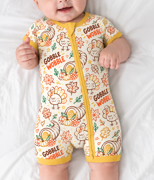 Baby lying down in the Gobble Wobble short sleeve bamboo zippy, showing turkeys, cornucopias and fall leaves on cream with a mustard two-way zip