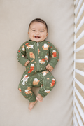 Smiling baby lying in a crib in the Meowy Christmas long sleeve bamboo zippy, olive green with ginger and white Christmas cats, stockings and gift boxes