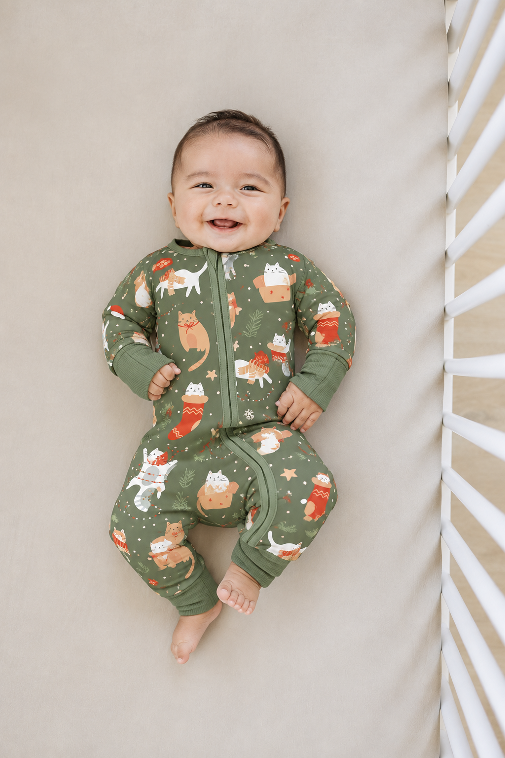 Smiling baby lying in a crib in the Meowy Christmas long sleeve bamboo zippy, olive green with ginger and white Christmas cats, stockings and gift boxes