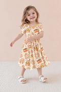 Smiling toddler girl twirling in the Gobble Wobble bamboo twirl dress, a cream Thanksgiving print with turkeys, cornucopias and fall leaves and a mustard neckline
