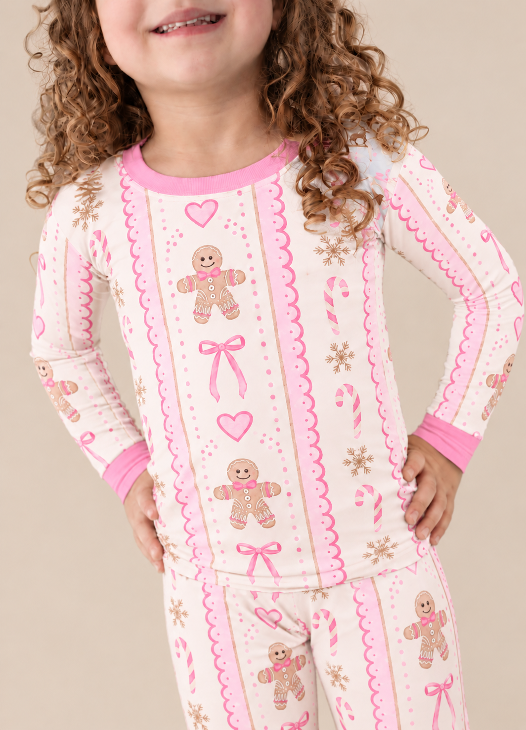Close-up of a child wearing the Pink Gingerbread bamboo pajama top with gingerbread men, pink bows, hearts and candy canes on cream