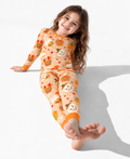 Smiling girl sitting on a white floor in the Gobble Apples long sleeve bamboo pajamas, with turkey and scarecrow caramel apples on camel and burnt orange cuffs