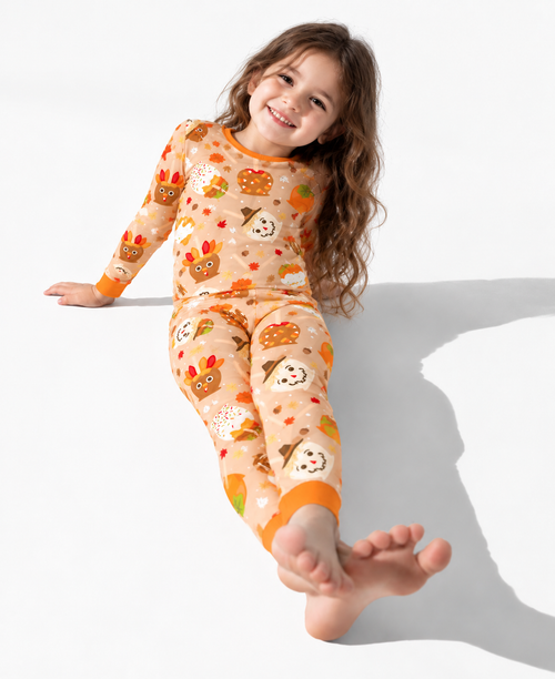 Smiling girl sitting on a white floor in the Gobble Apples long sleeve bamboo pajamas, with turkey and scarecrow caramel apples on camel and burnt orange cuffs