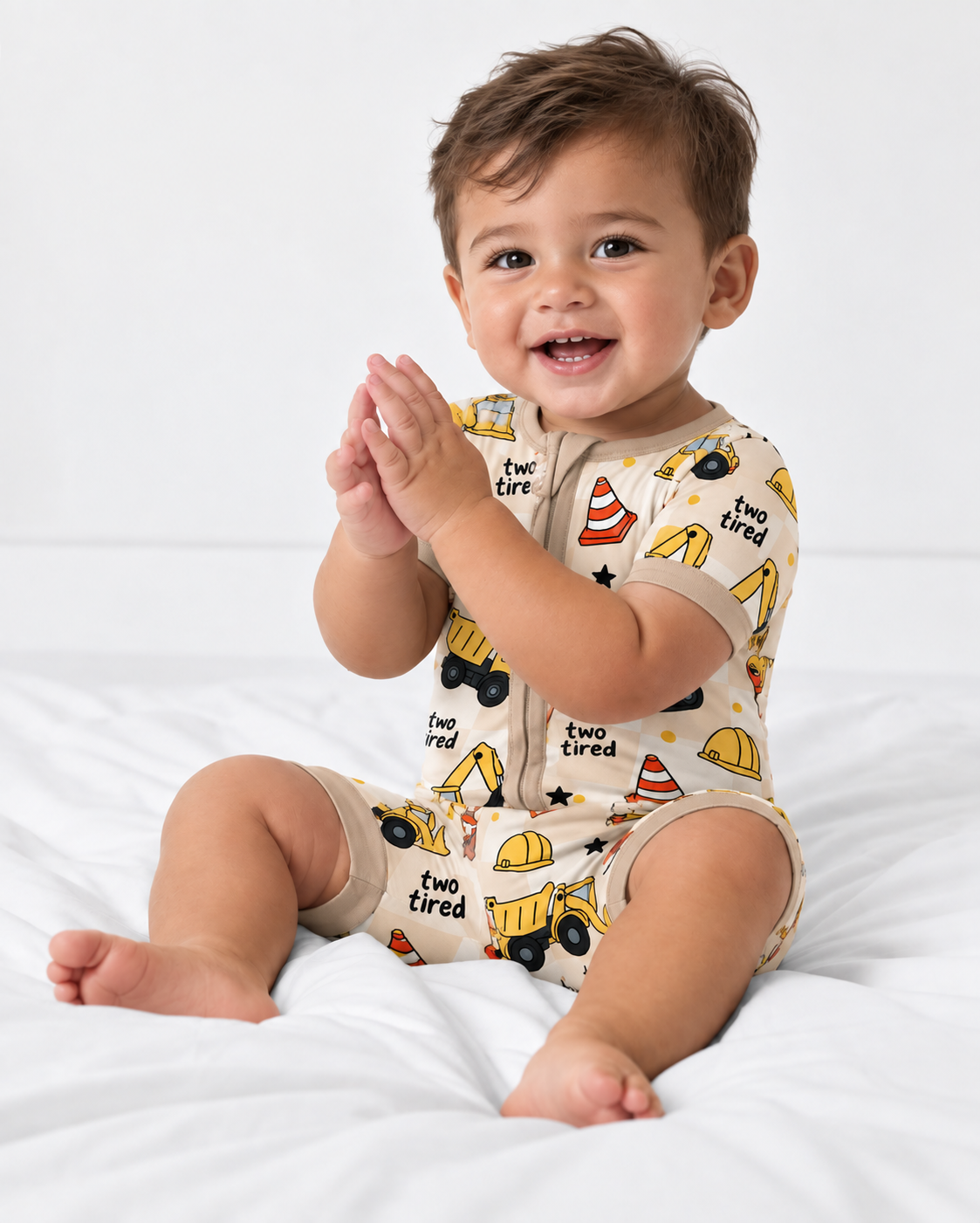 Toddler wearing a construction print bamboo short zippy for a 2nd birthday, with yellow trucks and "two tired" lettering