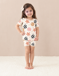 Girl wearing Merry & Bright short sleeve bamboo pajamas with checkerboard ornaments, blush and gold baubles and pink-striped stars on cream, with beige trim.