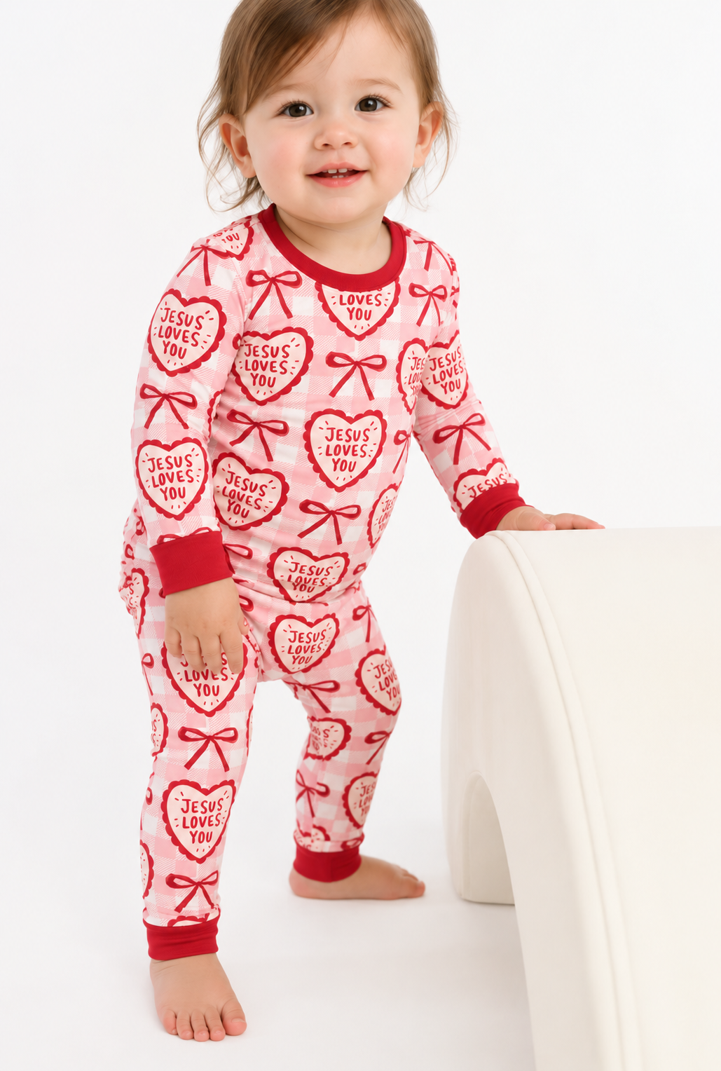 Toddler in Jesus Loves You long sleeve bamboo pajamas with cream hearts and red bows on pink gingham, red cuffs