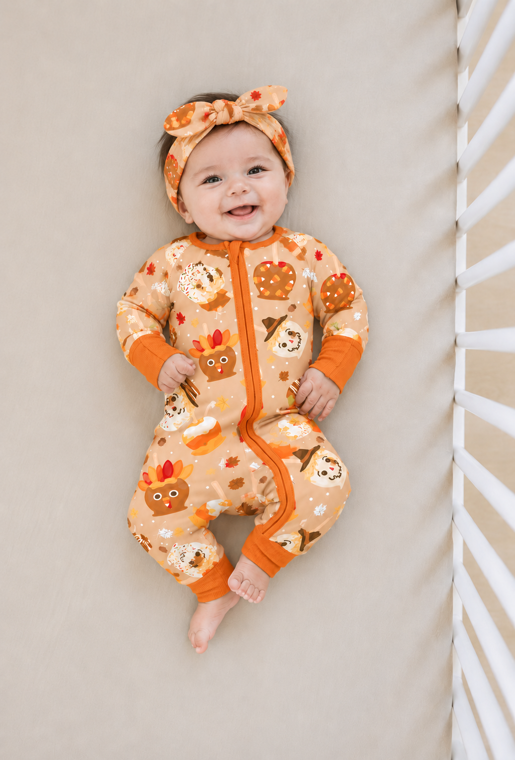 Smiling baby in a crib wearing the Gobble Apples bamboo bow headband with the matching caramel apple zippy