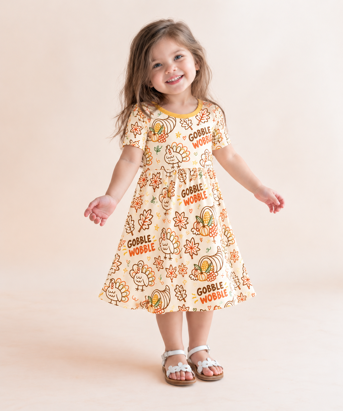 Toddler girl in the Gobble Wobble short sleeve bamboo dress with doodled turkeys and orange and brown Gobble Wobble lettering on cream