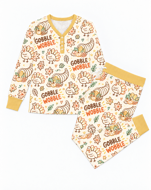Flat lay of the Gobble Wobble women's pajama set: long sleeve button henley top and drawstring joggers in a cream turkey print with mustard cuffs