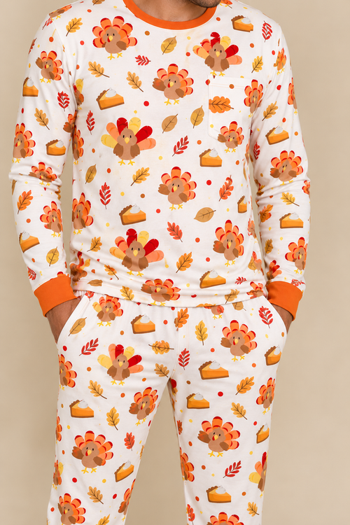 Man wearing the Turkey & Pie men's long sleeve bamboo pajama set, cream with turkeys, pumpkin pie and autumn leaves, chest pocket and orange ribbed cuffs