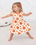 Toddler girl twirling in the Turkey & Pie bamboo twirl dress, cream with turkeys, pumpkin pie slices and autumn leaves, orange trim at neck and sleeves