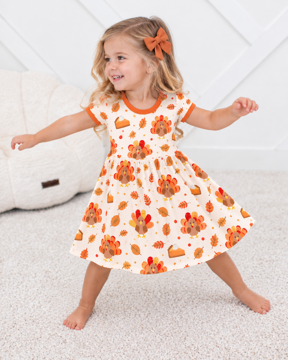 Toddler girl twirling in the Turkey & Pie bamboo twirl dress, cream with turkeys, pumpkin pie slices and autumn leaves, orange trim at neck and sleeves