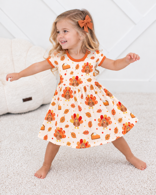 Toddler girl twirling in the Turkey & Pie bamboo twirl dress, cream with turkeys, pumpkin pie slices and autumn leaves, orange trim at neck and sleeves