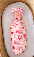 Newborn wrapped in the Little Texan bamboo swaddle blanket with matching bow headband, pink cowgirl boots and red roses on cream