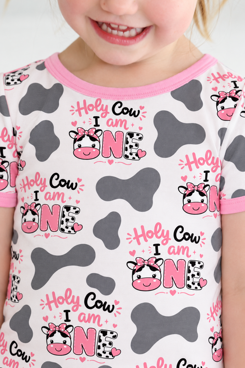 Toddler girl in a Holy Cow I'm One short sleeve bamboo pajama set with cow print and pink trim
