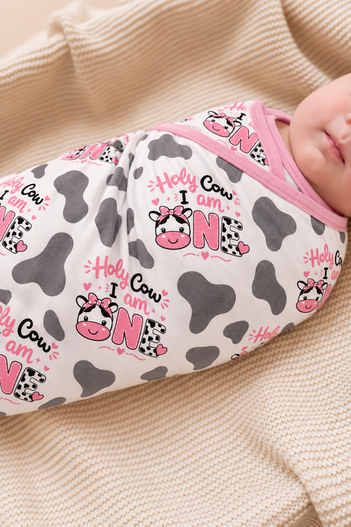 Baby wrapped in a Holy Cow I'm One cow print bamboo blanket with grey spots and pink cows