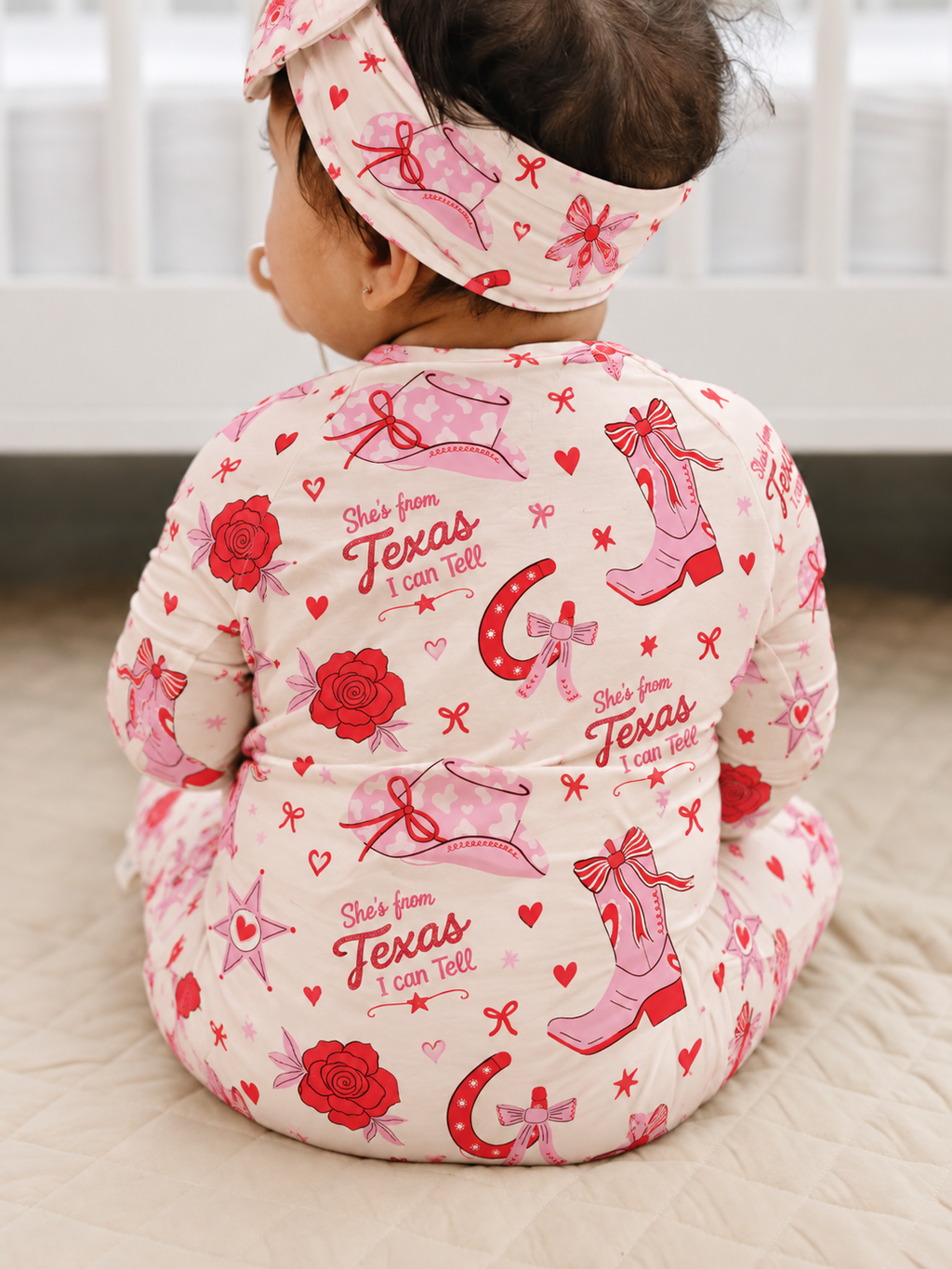 Baby in the matching Little Texan bamboo zippy and head wrap, back view of the pink cowgirl boots and red roses print