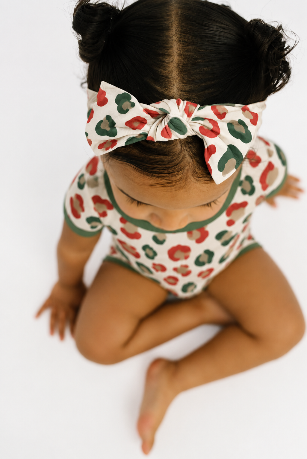 Toddler seen from above wearing the Christmas Leopard bow headband with a matching short sleeve romper