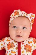 Toddler girl wearing the Turkey & Pie bamboo bow headband with a big bow, cream with turkeys and autumn leaves, paired with the matching zippy with orange zipper