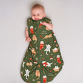 Baby lying in an olive green Meowy Christmas bamboo sleep sack printed with ginger and white cats in stockings and gift boxes