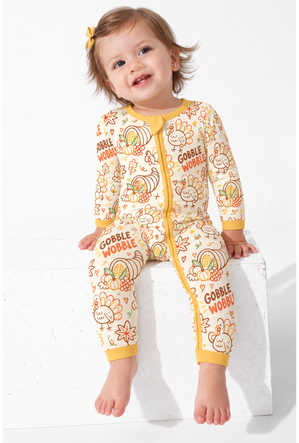 Smiling toddler in the Gobble Wobble long sleeve bamboo zippy, a cream turkey and cornucopia print with a mustard two-way zip and ribbed cuffs