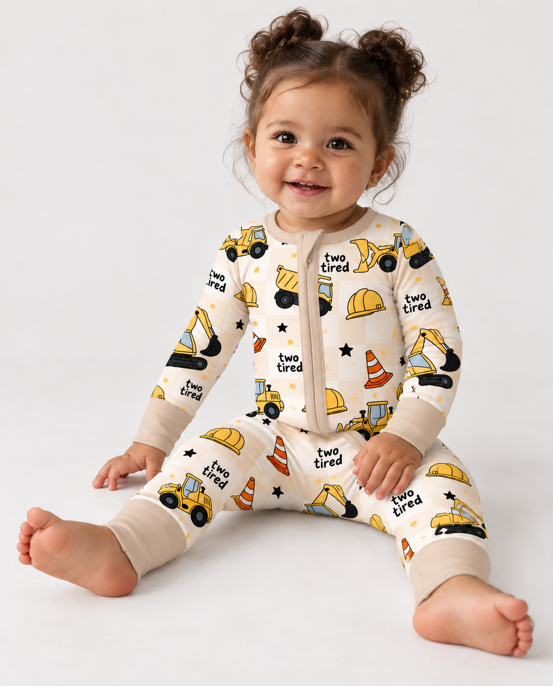 Toddler wearing a construction print bamboo zippy for a 2nd birthday, with yellow trucks and "two tired" lettering