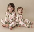 Big sister and toddler sitting together in Christmas Tree bamboo pajamas with sage green and pink trees, red bows and sage green cuffs