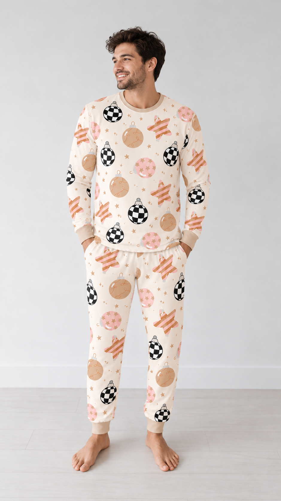 Man wearing the Merry & Bright men's bamboo pajama set with checkerboard ornaments, blush and gold baubles and striped stars on cream