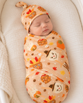 Newborn wrapped in the Gobble Apples bamboo swaddle blanket, a camel print of turkey, scarecrow and candy corn caramel apples with fall leaves and acorns.