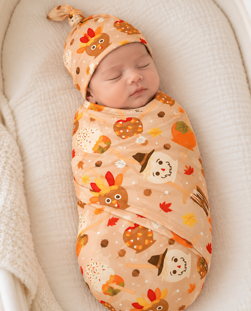 Newborn wrapped in the Gobble Apples bamboo swaddle blanket, a camel print of turkey, scarecrow and candy corn caramel apples with fall leaves and acorns.