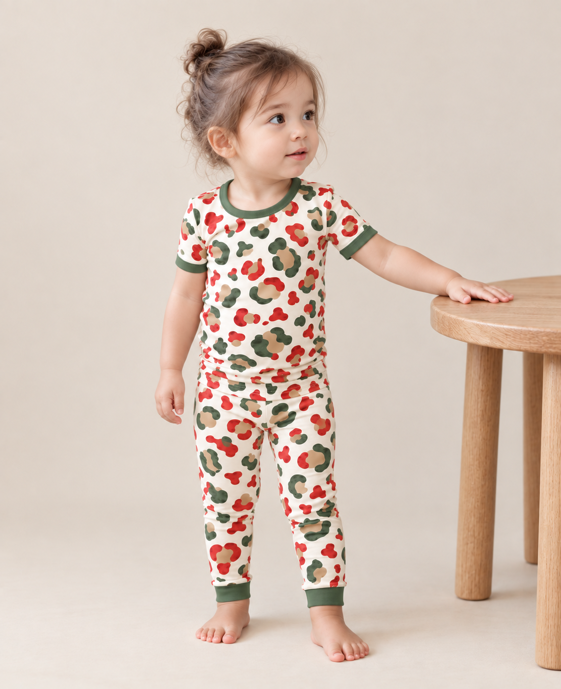 Toddler girl in Christmas Leopard short sleeve bamboo pajamas with long cuffed pants, red, green and gold spots on cream with pine green trim