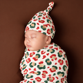 Sleeping newborn wearing a Christmas Leopard bamboo knot hat, swaddled in the matching red, green and gold spotted blanket